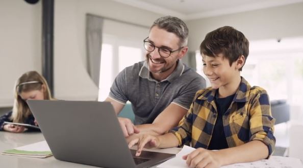 Father and son smiling looking at laptop with daughter looking at tablet